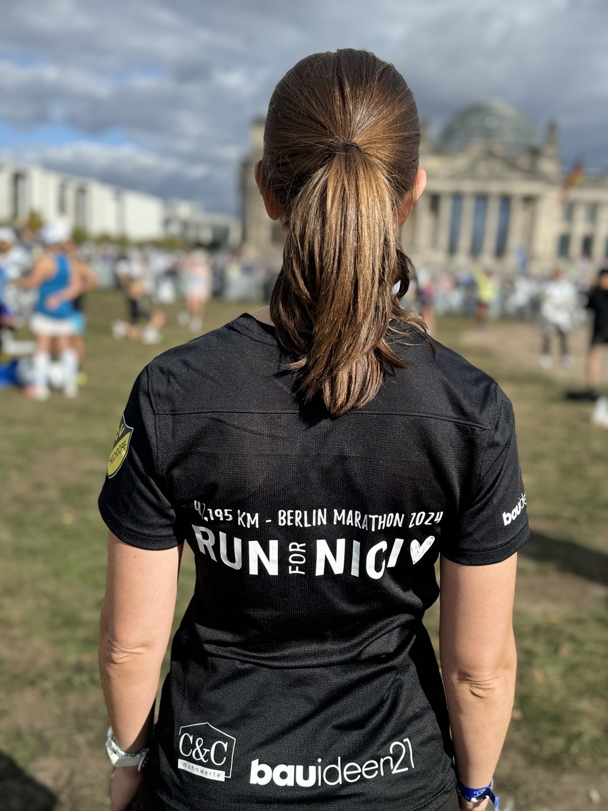 Carina von hinten vor dem Reichstag, auf dem Rücken ihres Shirts steht 42,195 km Berlin Marathon 2024 und Run for Nici