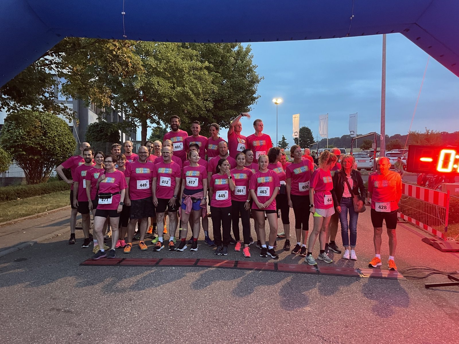 Das Team in pinken Shirts steht in der Dämmerung unter dem Startbogen des Bietigheimer Fackellaufs