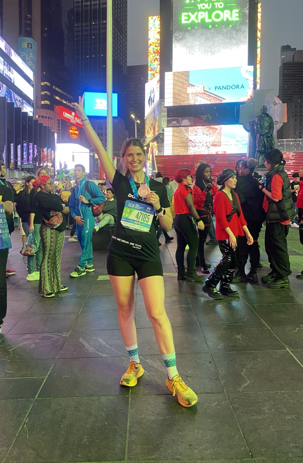 Carina steht nach dem New-York-Marathon 2022 mit der Medaille um den Hals am Times Square und streckt den Arm nach oben