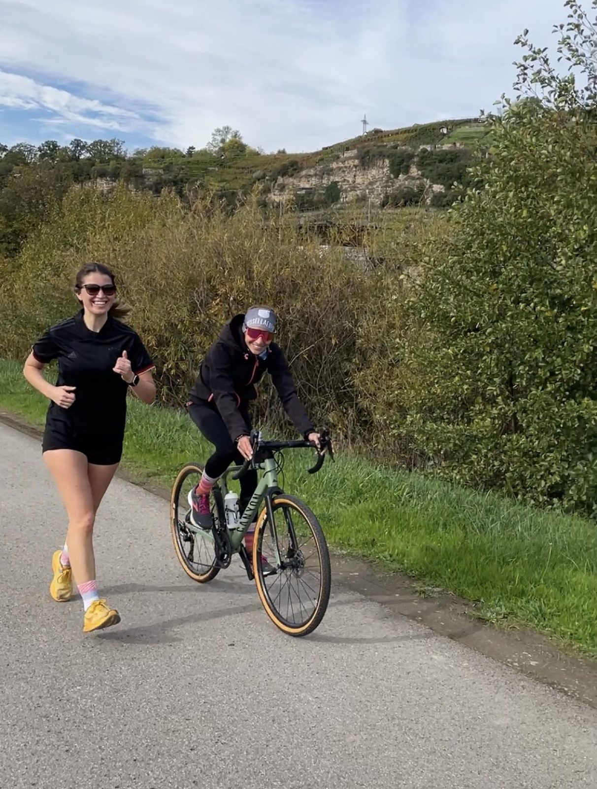 Carina läuft auf einem Feldweg, daneben fährt jemand mit dem Rennrad und hält das Tempo